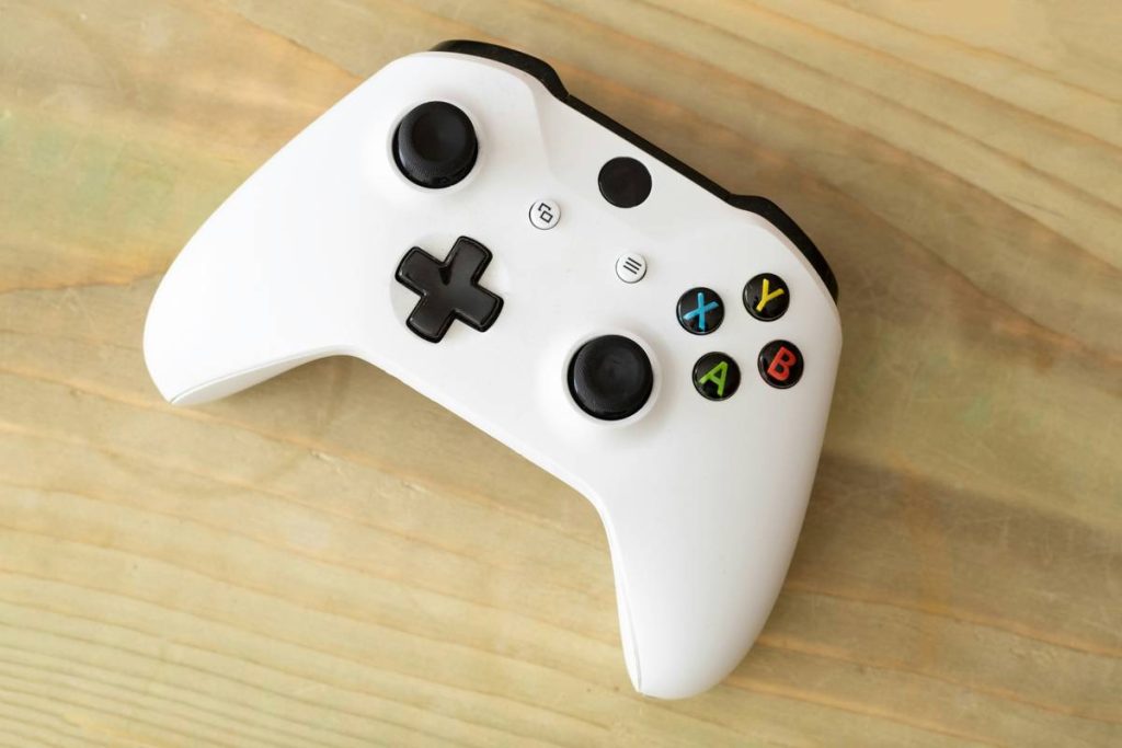 A white unbranded Xbox One wireless controller on a light wood background.